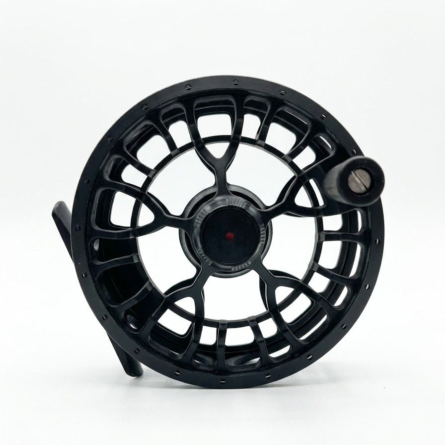 A black fly fishing reel with a complex cutout frame design and a small silver knob, photographed on a seamless white background.