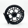 A black fly fishing reel with a complex cutout frame design and a small silver knob, photographed on a seamless white background.